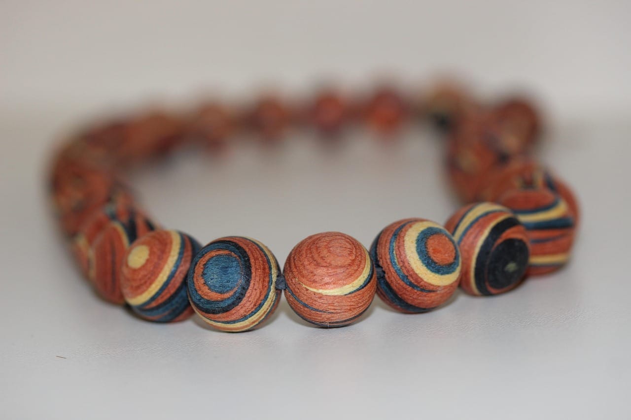 Gros plan sur un collier composé de perles de bois colorées. Les perles présentent des motifs tourbillonnants rouges, bleus et beiges.