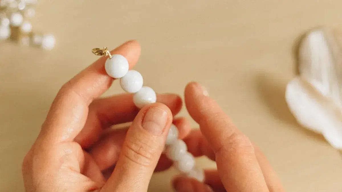 Gros plan de mains enfilant des perles blanches sur un fil à bijoux.