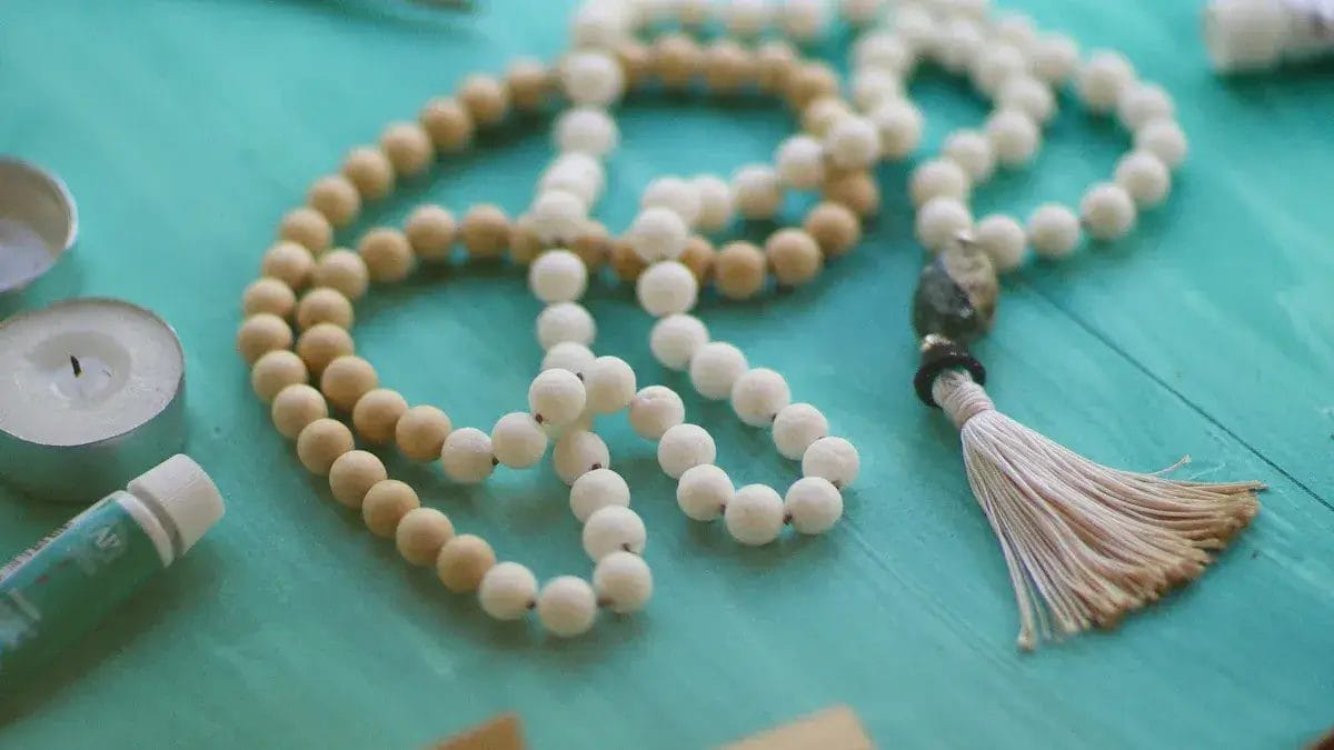 Collier mala en perles avec perles en bois blanc crème et beige et un pompon.