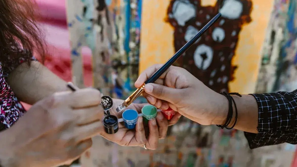 Deux mains peignent avec un pinceau et des petits pots de peinture.