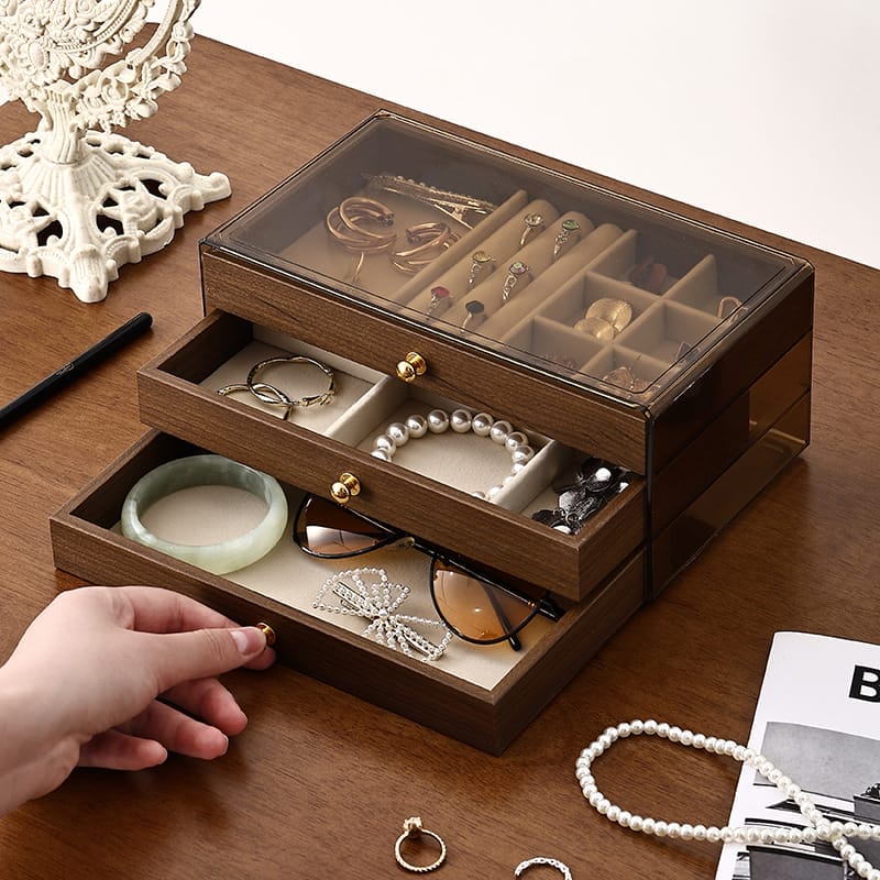 Boîte à bijoux en bois à trois niveaux avec plateau en verre, rempli de colliers, de boucles d'oreilles et de lunettes de soleil.